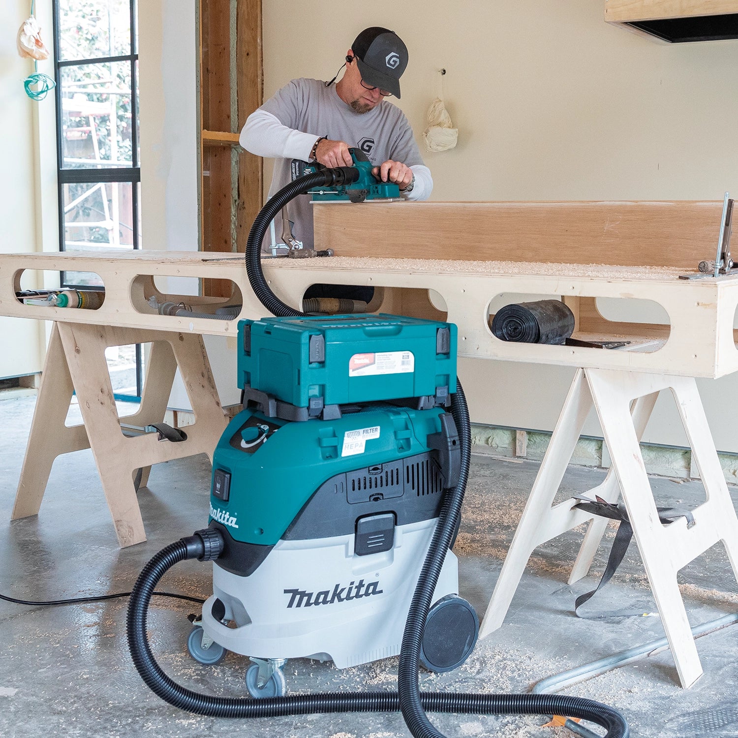 Woodworker using handheld Makita planer connected to Makita VC4210L HEPA dust extractor during cabinetry work