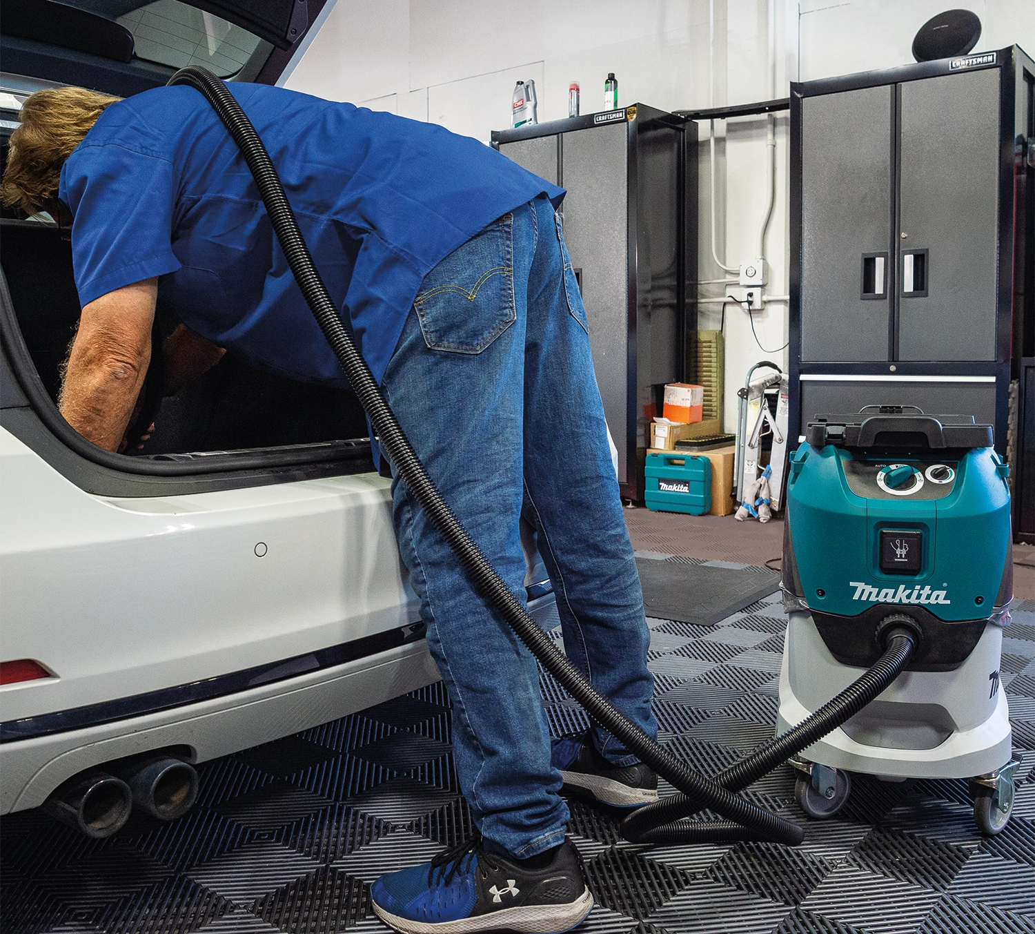 Technician using Makita VC4210L dust extractor to vacuum the interior of a white vehicle in a garage setting