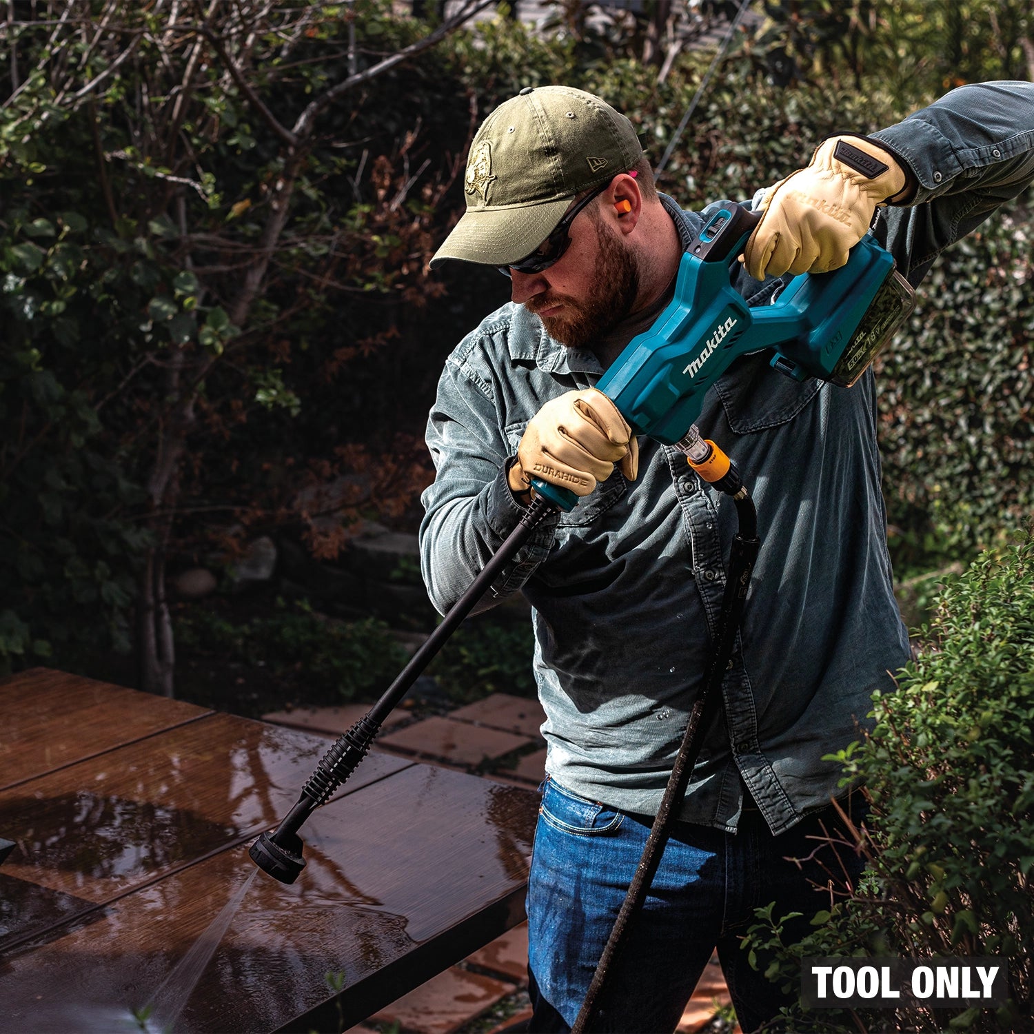 Man using a Makita power washer on a wooden surface with trees in the background