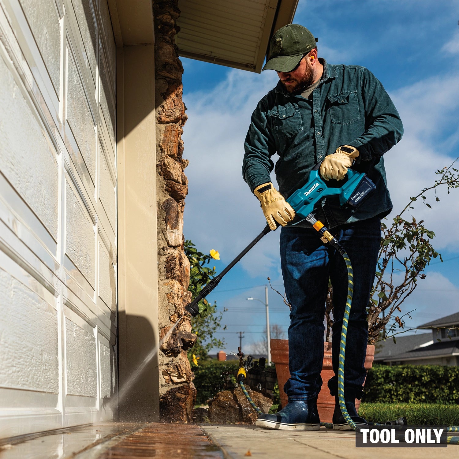 Person using a pressure washer tool on a house exterior with a clear blue sky.