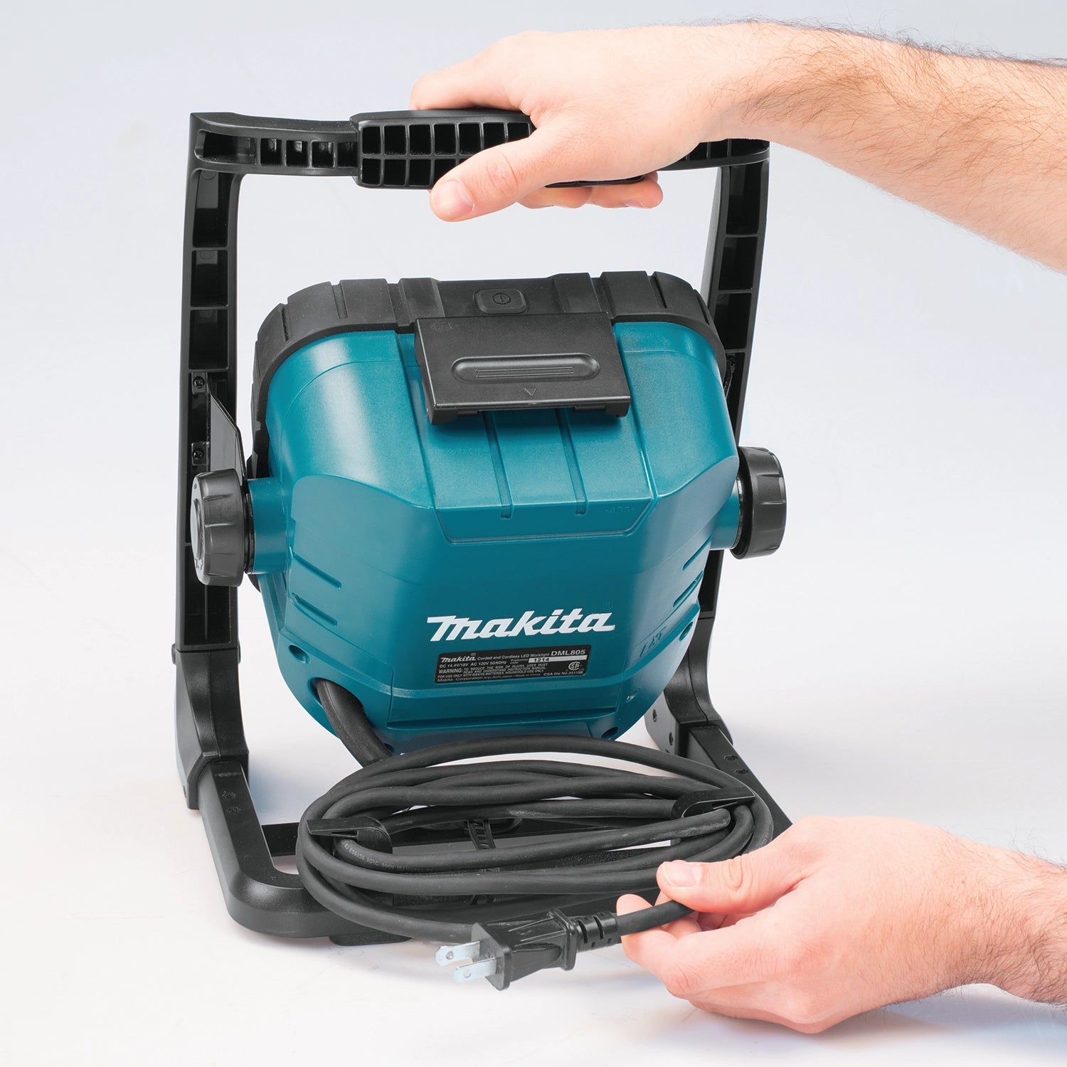 technician adjusting makita led work light with hands on back panel
