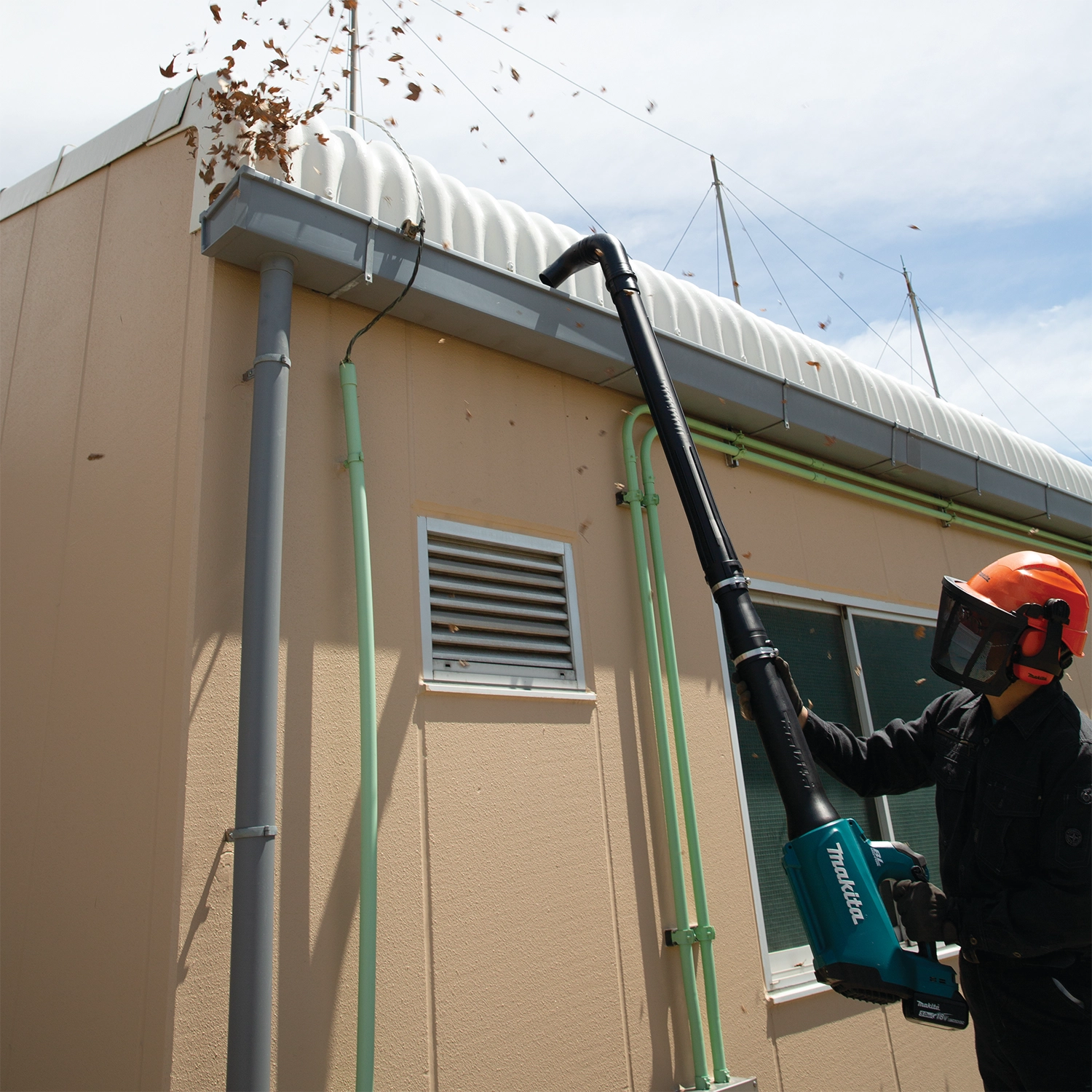 makita blower with gutter cleaning kit in active use clearing leaves from residential gutter
