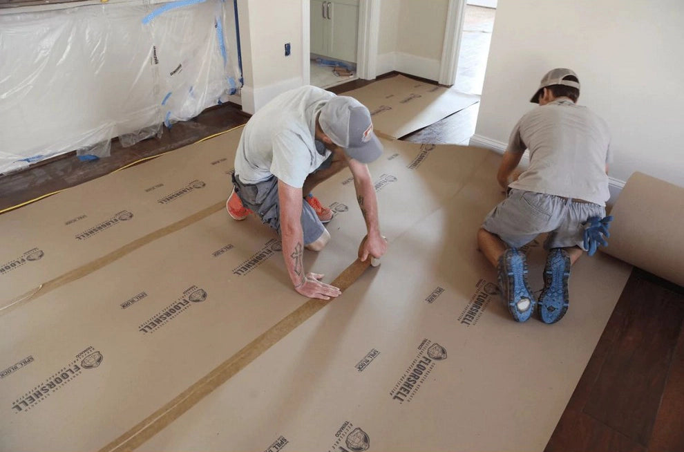 Two installers securing overlapping Floor Shell boards using Trimaco seam tape during setup
