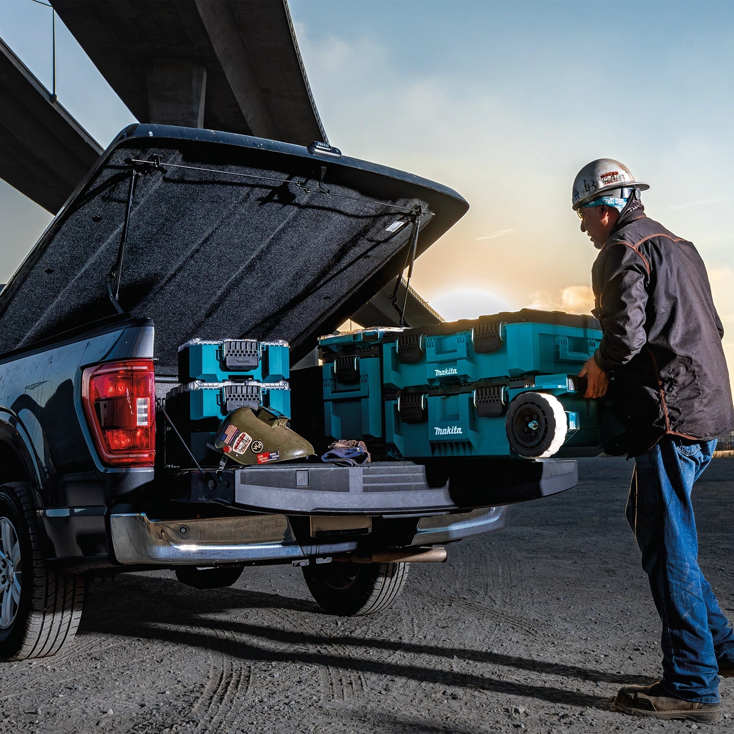 Worker loading Makita MAKTRAK storage boxes into truck bed at jobsite
