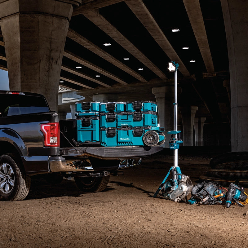 Makita MAKTRAK modular toolboxes stacked in a truck bed at a nighttime jobsite under a highway overpass, with cordless power tools and a work light nearby.

