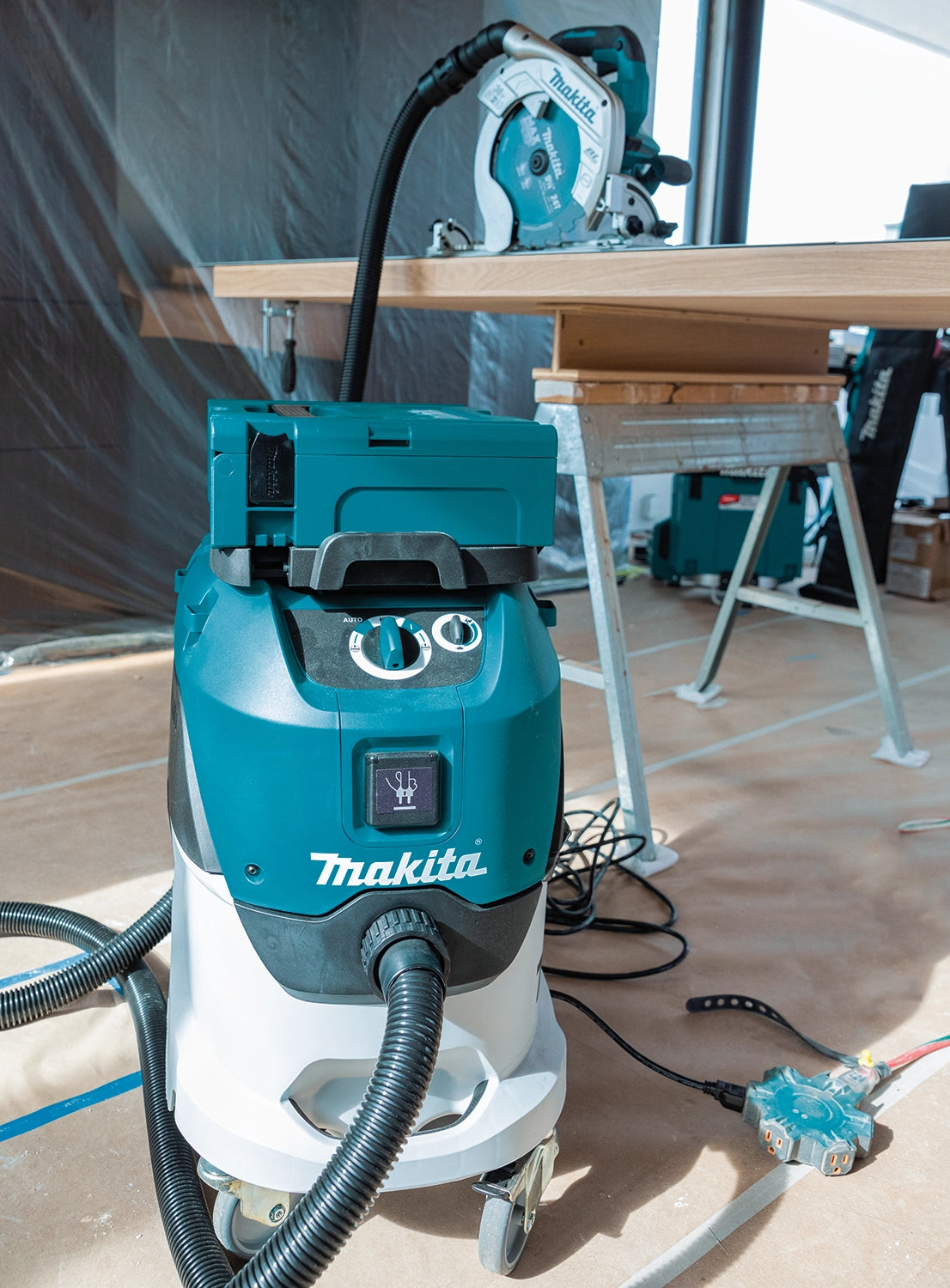 Makita VC4210L dust extractor connected to circular saw on a construction jobsite with drop cloth flooring

