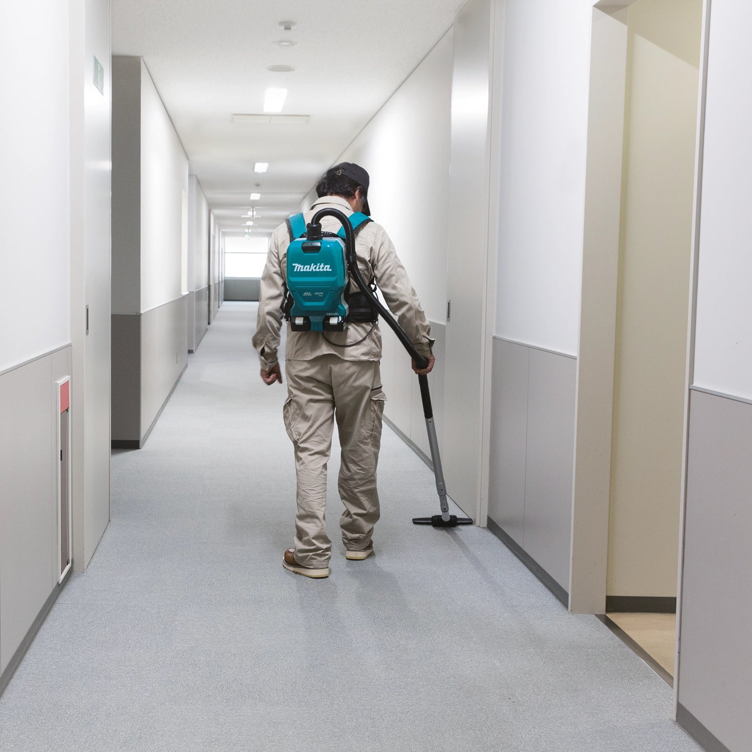 Makita backpack vacuum cleaning school hallway with operator walking
