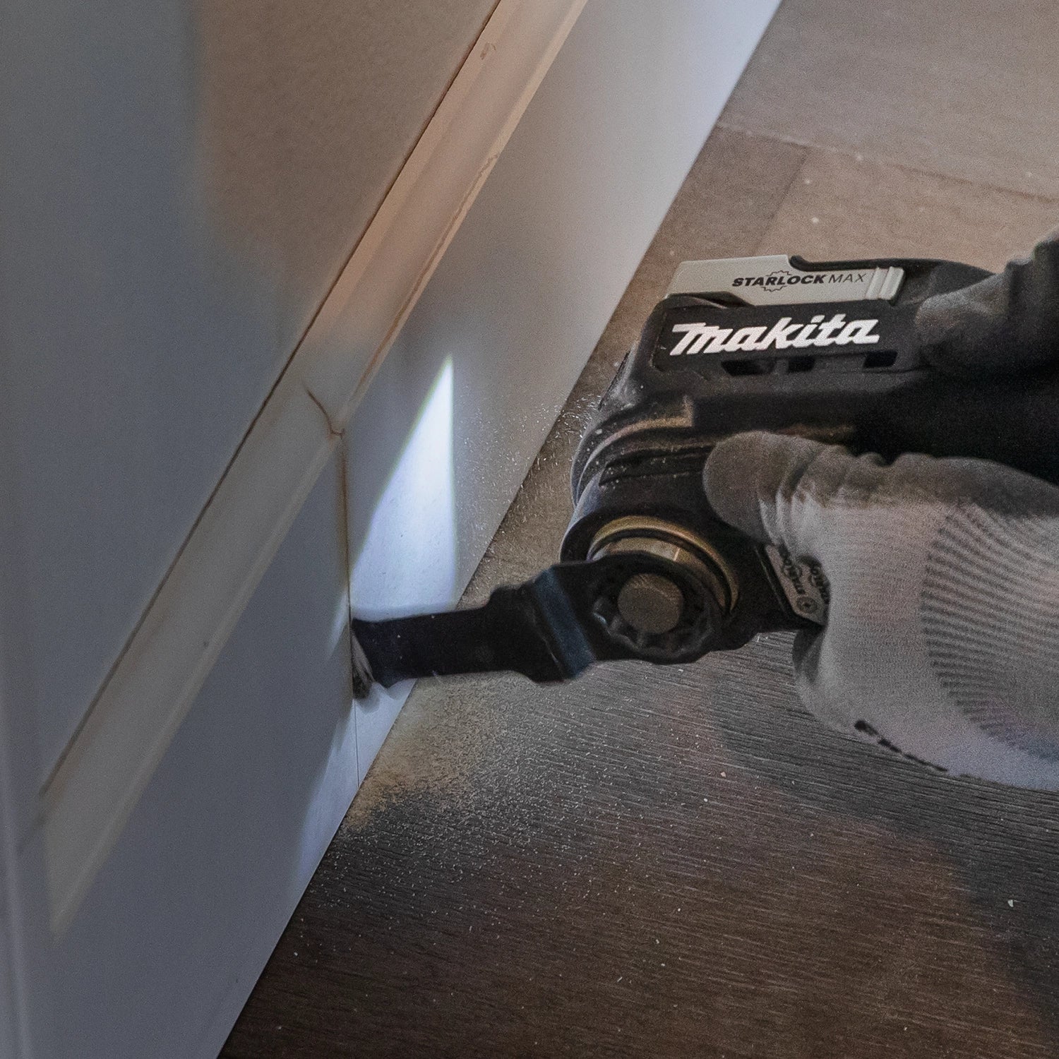Makita multi-tool flush-cutting wood trim along baseboard

