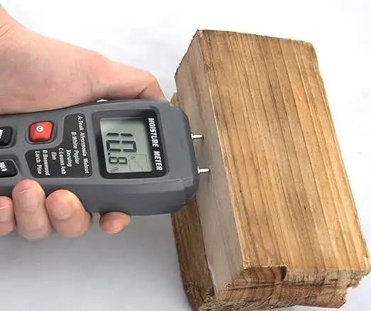 digital moisture meter testing moisture level in a piece of stacked firewood
