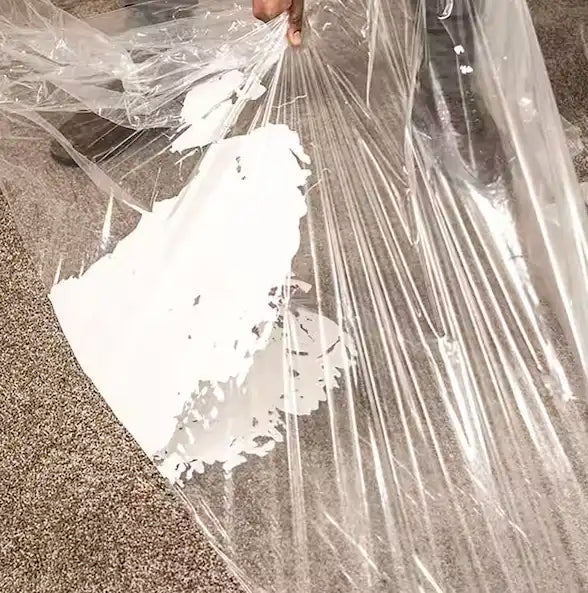 Presto carpet film peeled back revealing clean carpet underneath dried paint splatter
