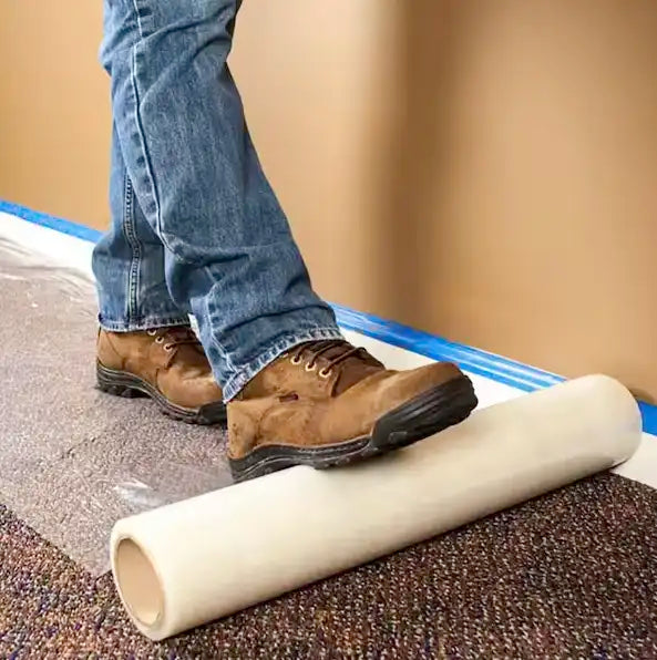 Carpet protection film being rolled along floor edge near wall for full coverage
