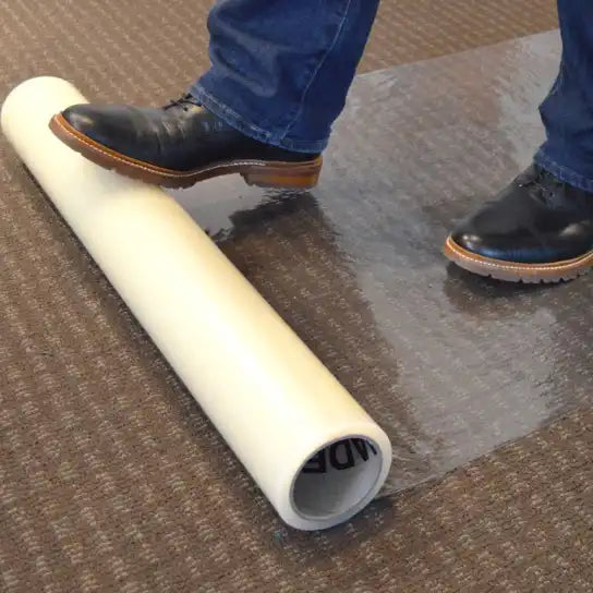 Worker rolling out Presto film on low-pile synthetic carpet during jobsite setup
