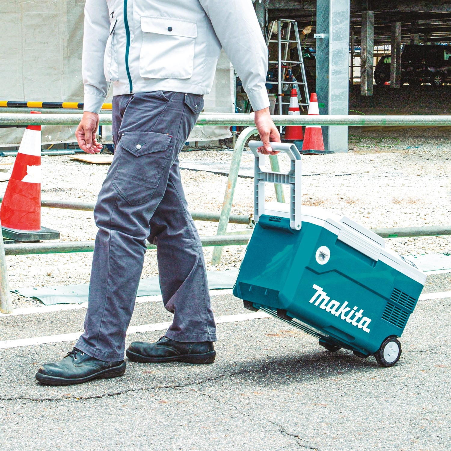 user pulling makita cooler warmer box on wheels across gravel path
