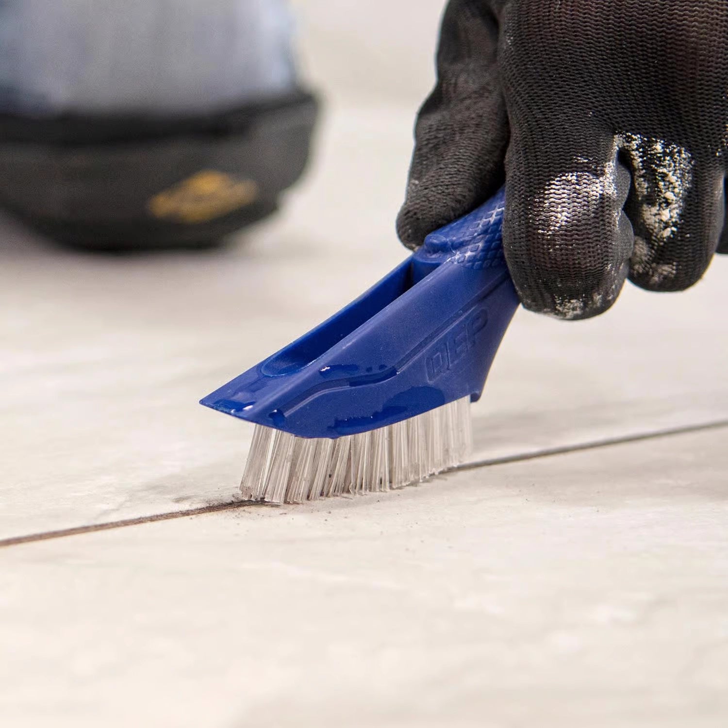 QEP Grout Cleaning Brush scrubbing grout lines on tiled surface
