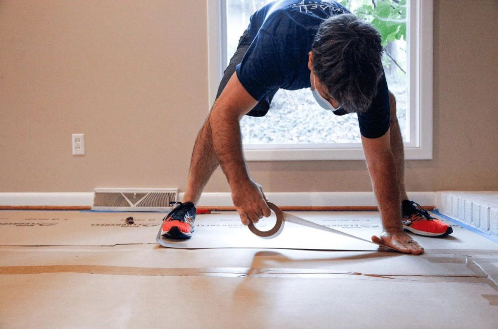 Worker stretching and applying Trimaco tape to Floor Shell board in home interior
