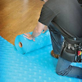 Contractor unrolling Trimaco AquaShield surface protector on floor for construction site preparation
