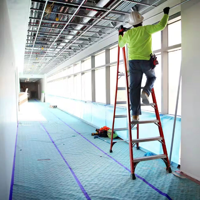 Contractor on ladder installing ceiling utilities with AquaShield protecting floor in hallway
