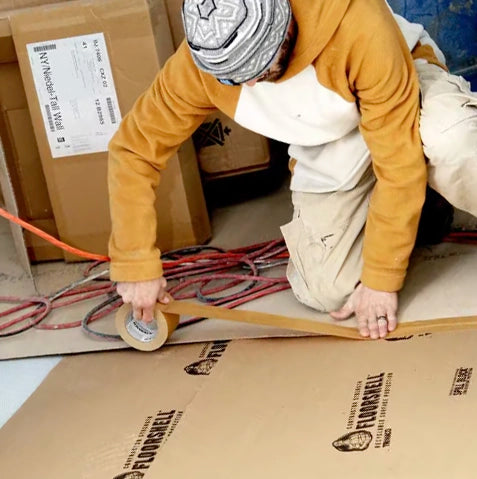 Contractor applying Trimaco seam tape to floor protection board during renovation setup
