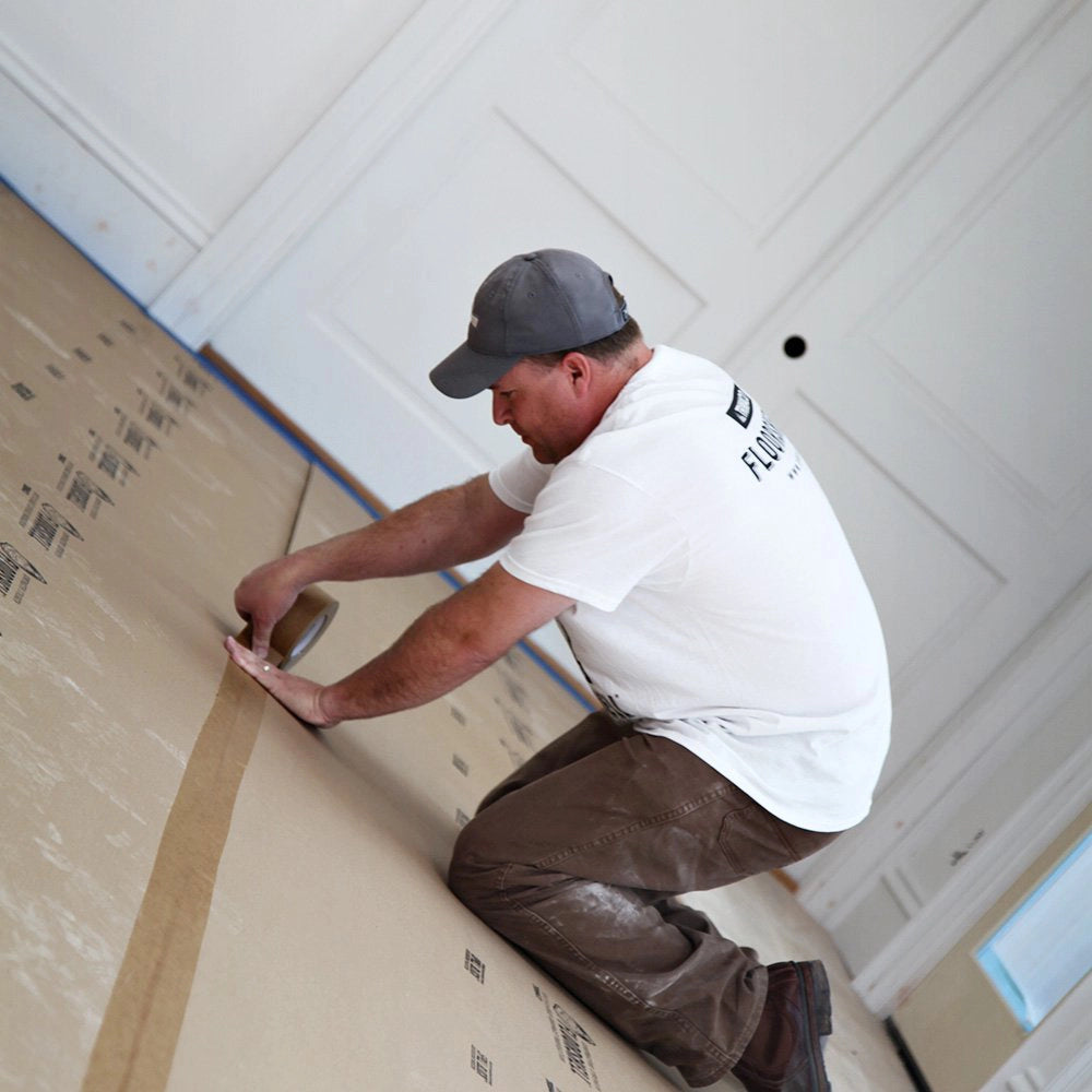 Trimaco seam tape being firmly applied along floor protection seams in a white interior space

