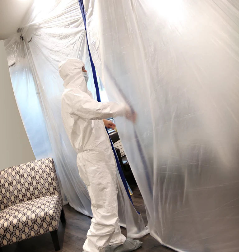 Worker in PPE suit opening zipper in plastic containment wall
